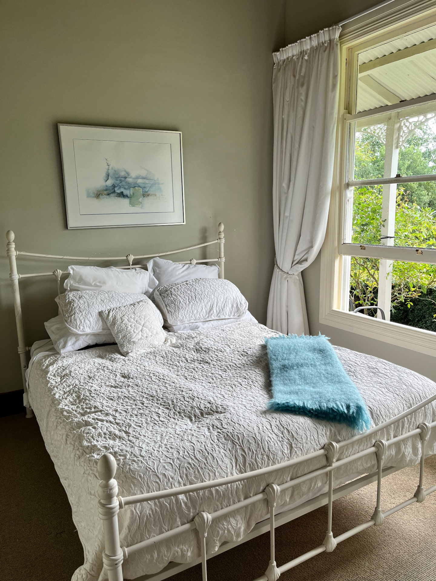 Master bedroom with white iron bed, sash window and morning light