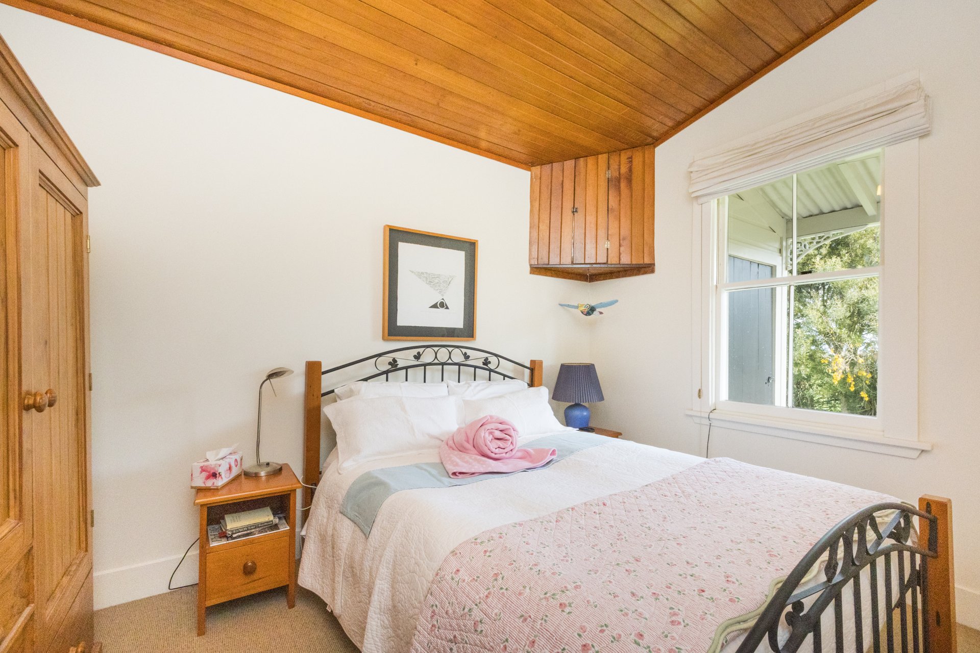 Second bedroom of the villa with a rimu timber ceiling, wrought-iron bed, quilt and folded pink blanket